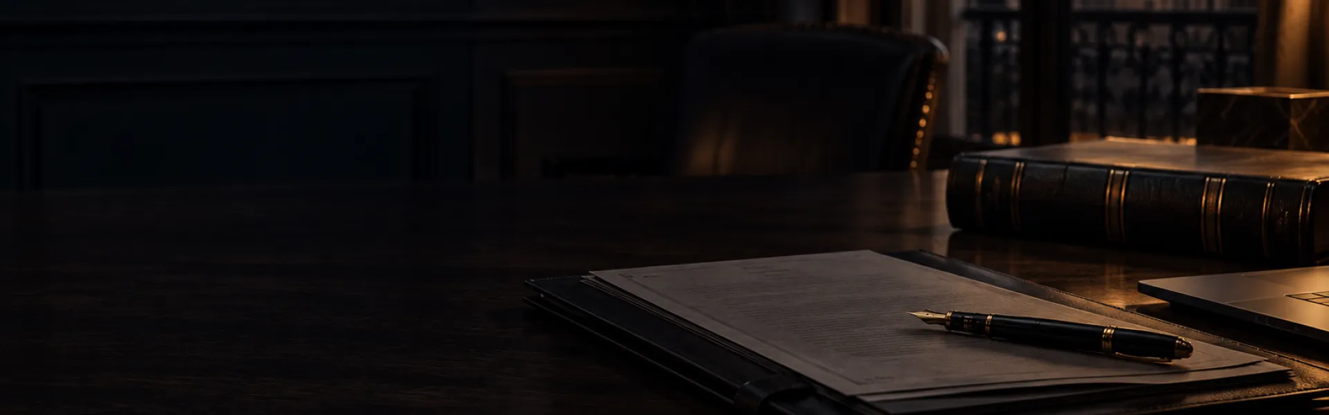 Documentación y pluma sobre una mesa de despacho en tonos oscuros