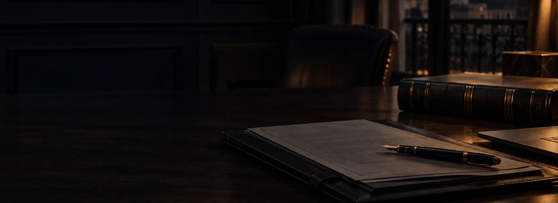 Documentación y pluma sobre una mesa de despacho en tonos oscuros